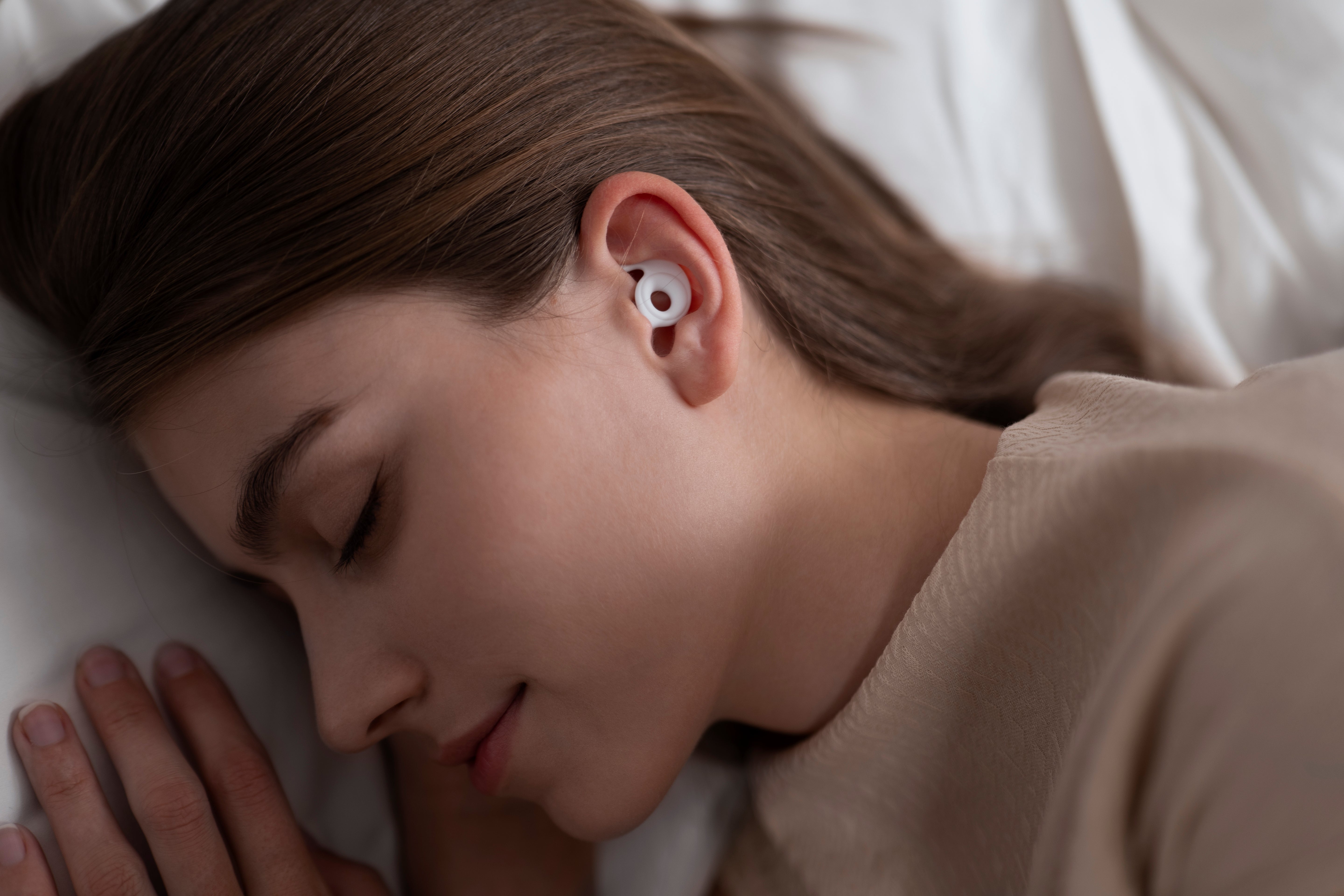 Woman sleeping with a white Best Sleep Earplugs for Side Sleepers. Block out the noise for all-night comfort and peace.
