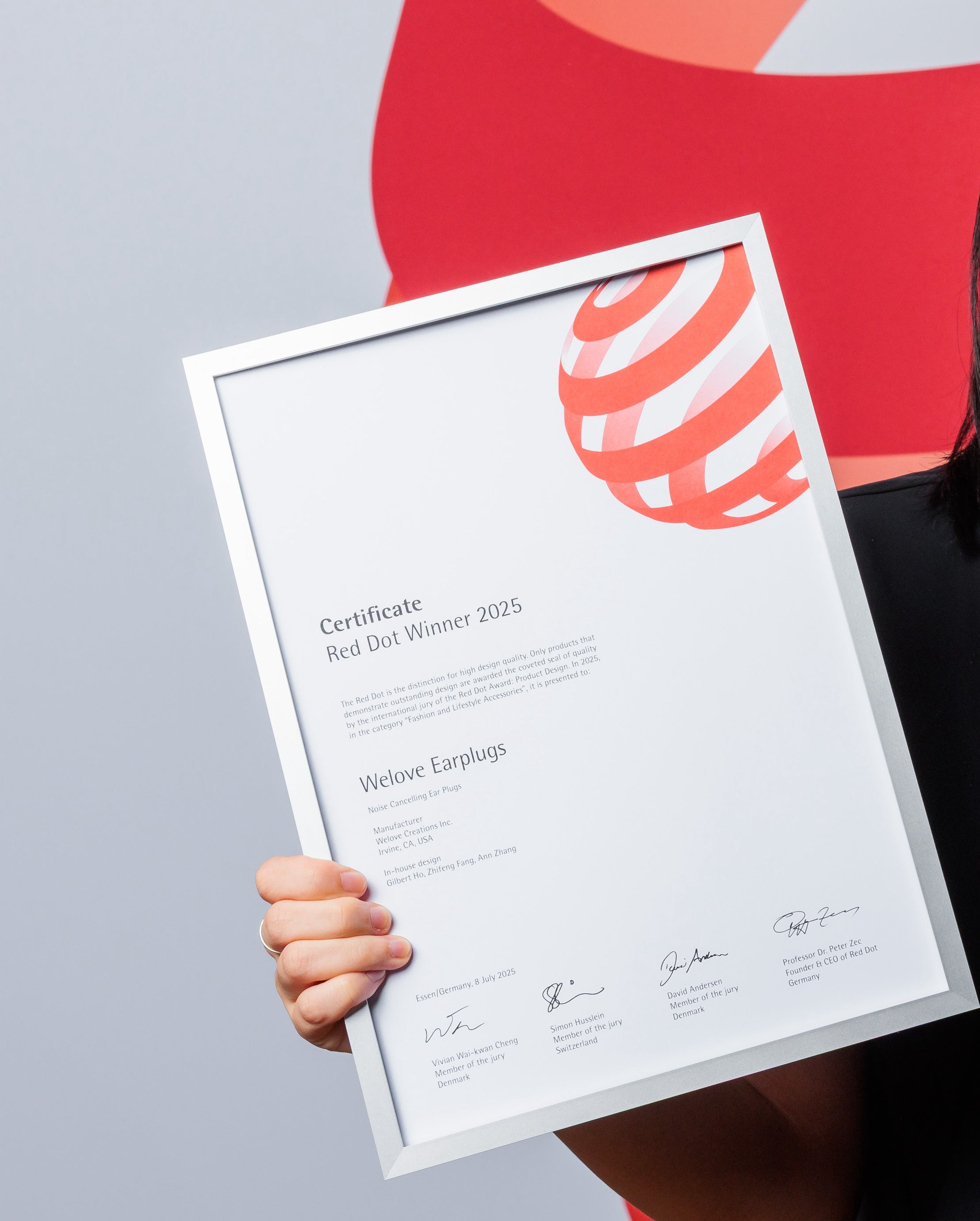 Person holding a framed certificate with a red dot design award 