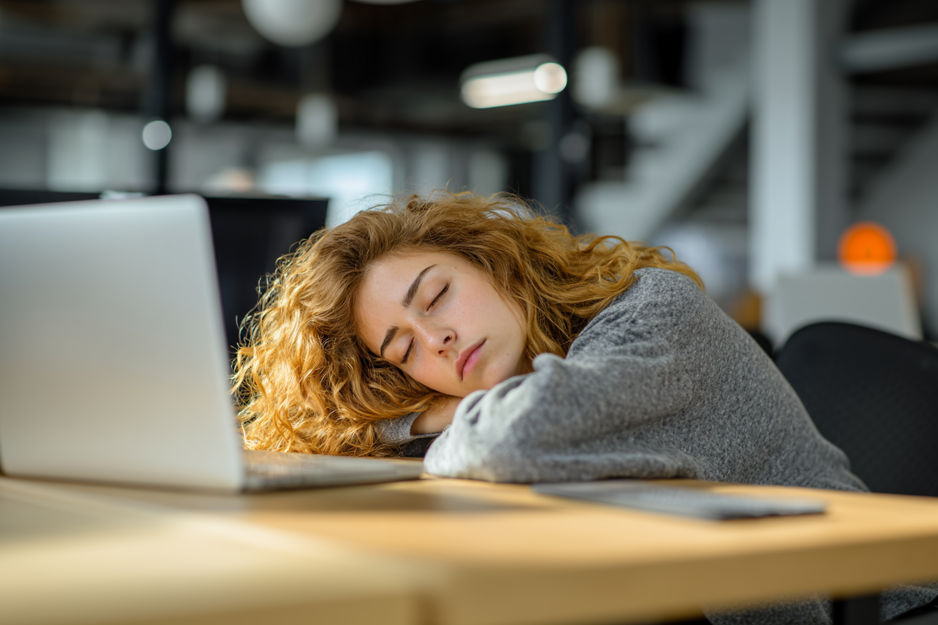 A lady taking a nap on a desk with a laptop in an office setting with Welove silicone noise canceling Earplugs for sleeping Red Dot winner 2025